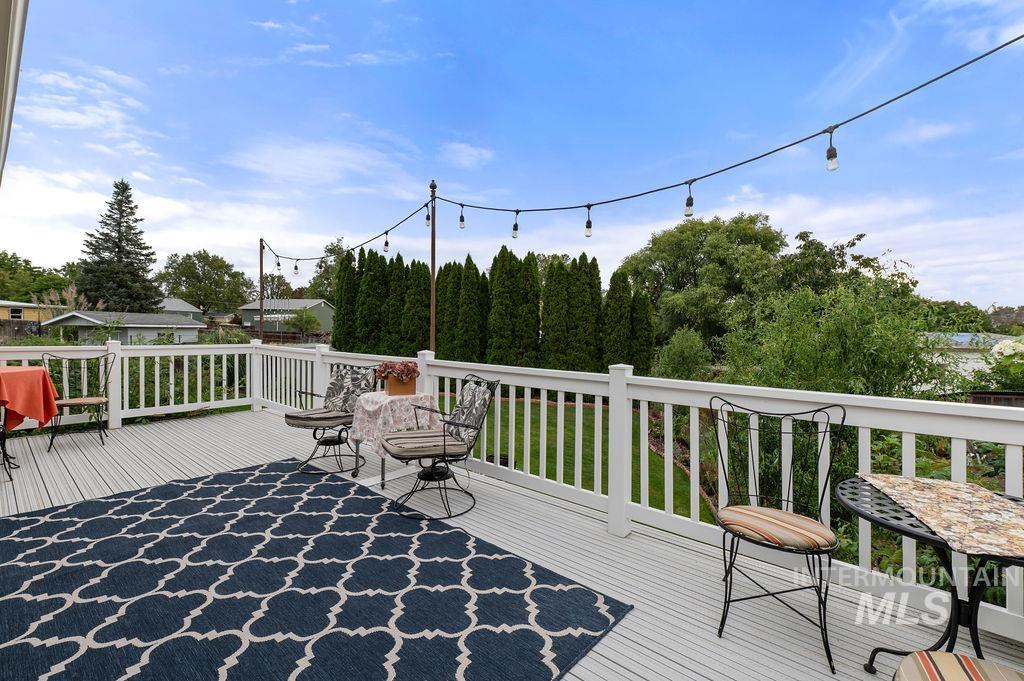 Furnished deck with a patterned rug, patio seating, white railing, and overhead string lights.