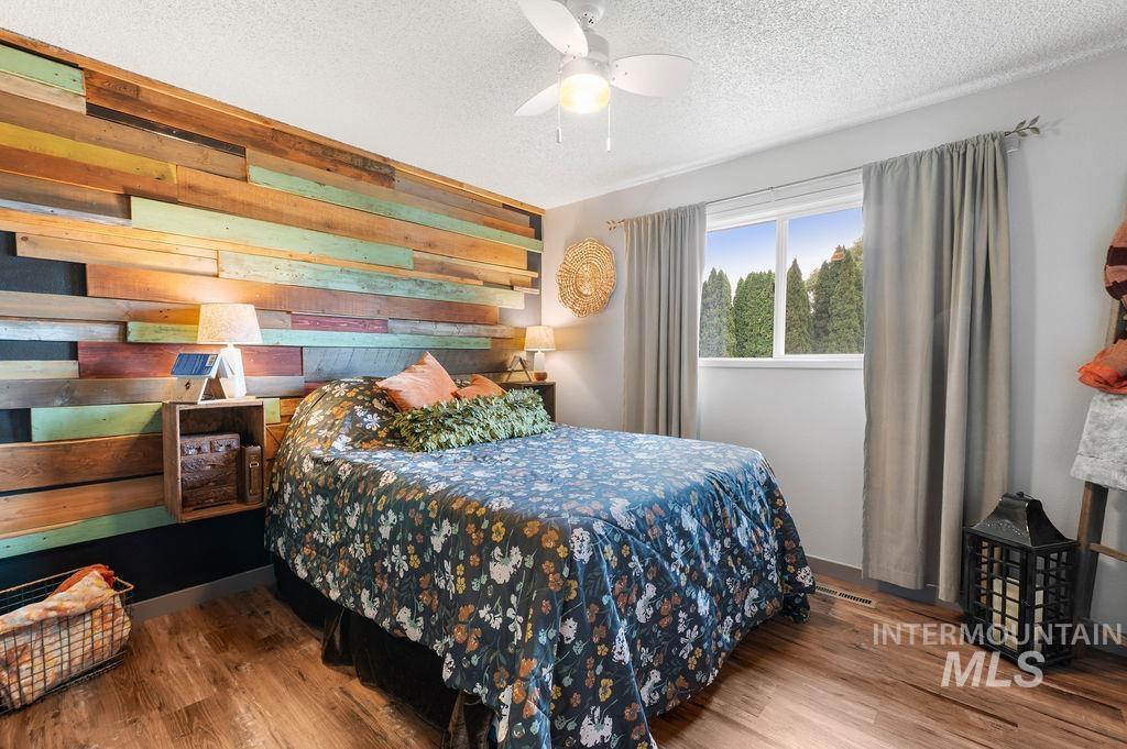 Bedroom with a colorful reclaimed-wood accent wall, floral bedding, and a window overlooking evergreen trees.