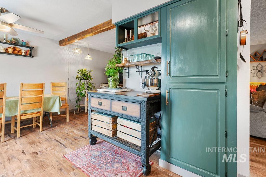 Kitchen with teal cabinetry, a wheeled island cart, wood floors, and an adjoining dining area.