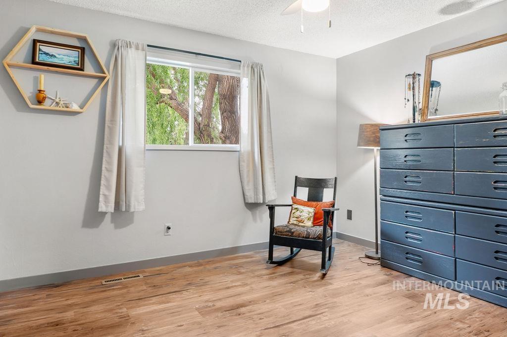 Bedroom with wood-look flooring, a curtained window, black rocking chair, and blue dresser.