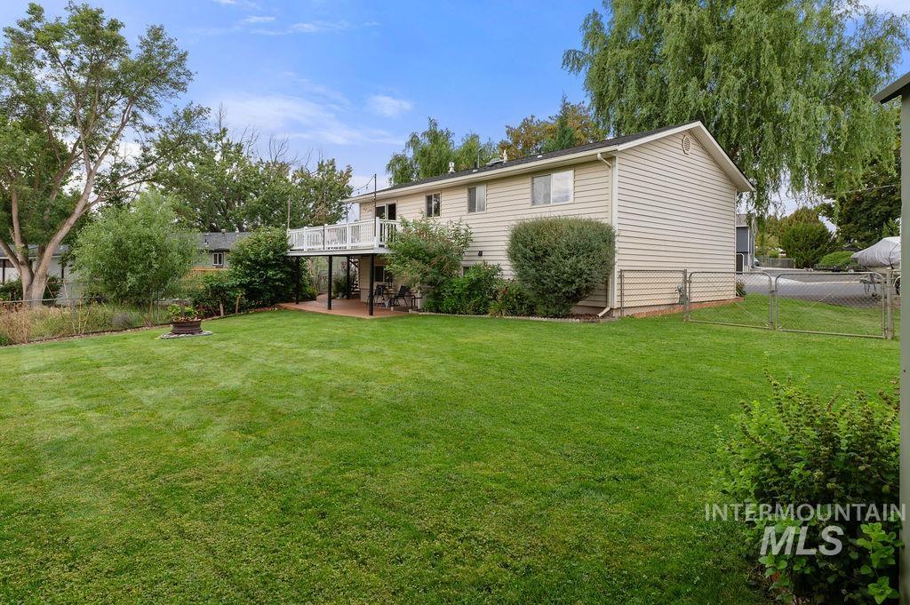 Rear of a beige split-level home with a raised deck overlooking a broad lawn and mature trees.