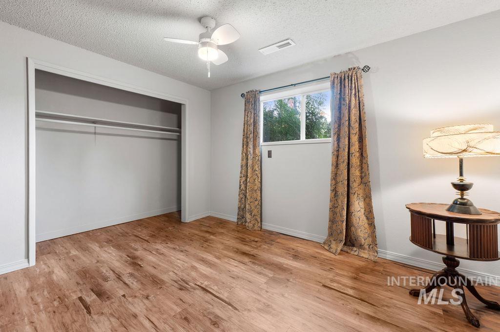 Bedroom with wood-look flooring, an open closet, curtained window, and ceiling fan.