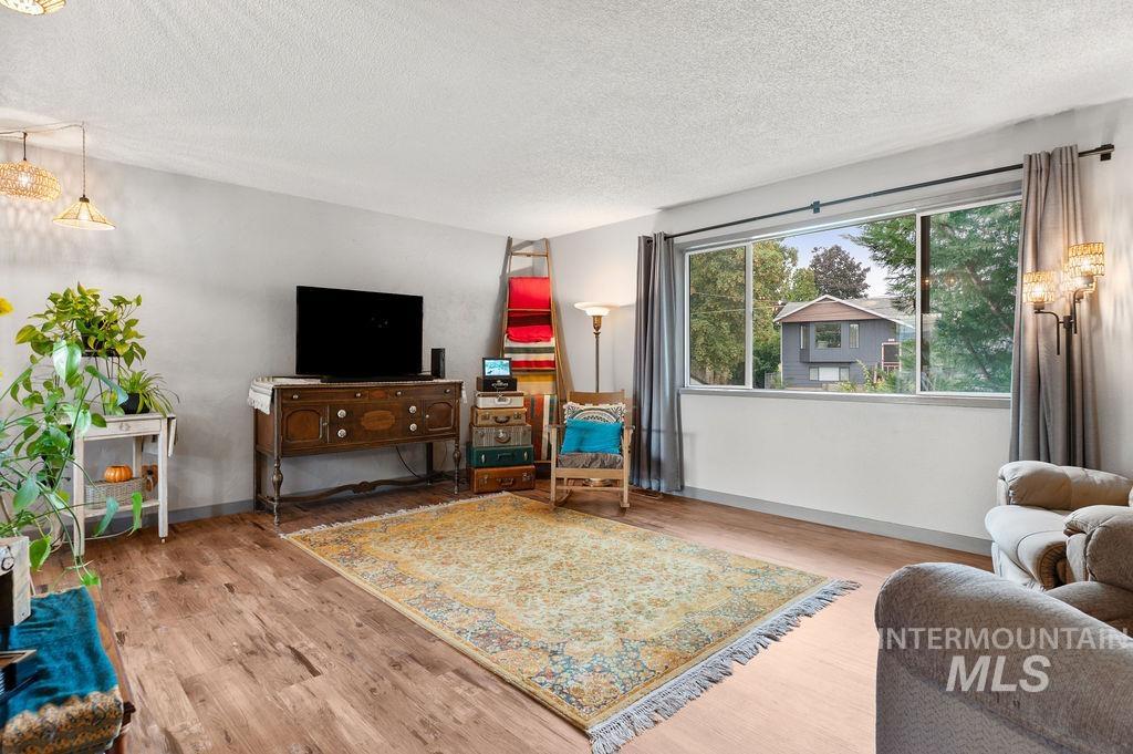 Living room with a vintage wooden console, patterned rug, and wide window overlooking trees and a neighboring home.