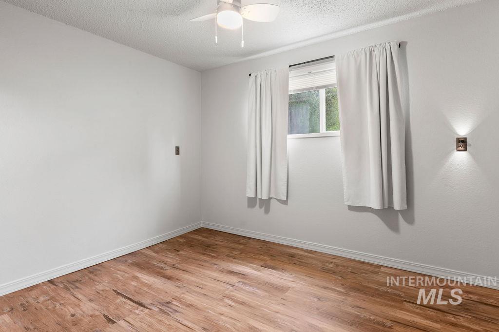 Empty bedroom with wood plank flooring, a curtained window, and a ceiling fan with light.