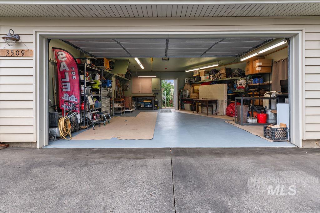 Open garage with a blue-gray floor, storage shelves along both walls, and a red FOR SALE flag.