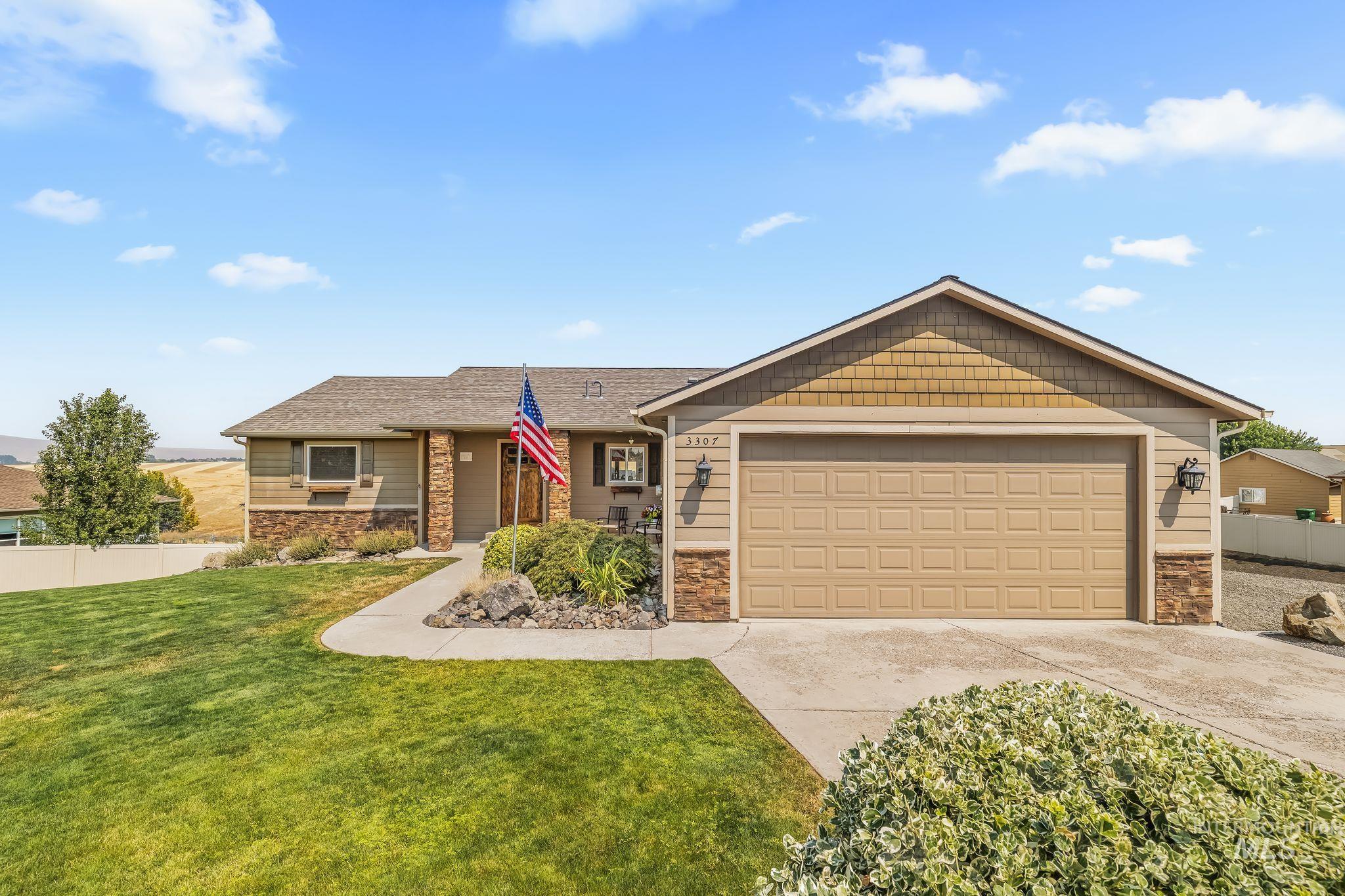 Single-story tan home with stone accents, double garage, green lawn, and an American flag.