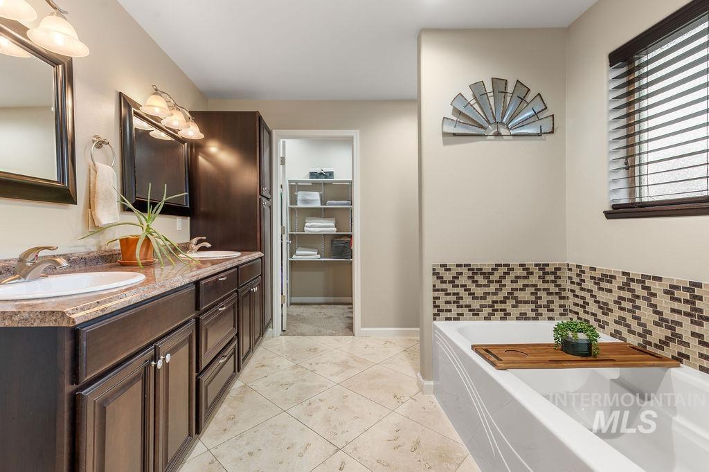 Bathroom with a double-sink vanity, white tub, mosaic tile surround, and open linen closet.