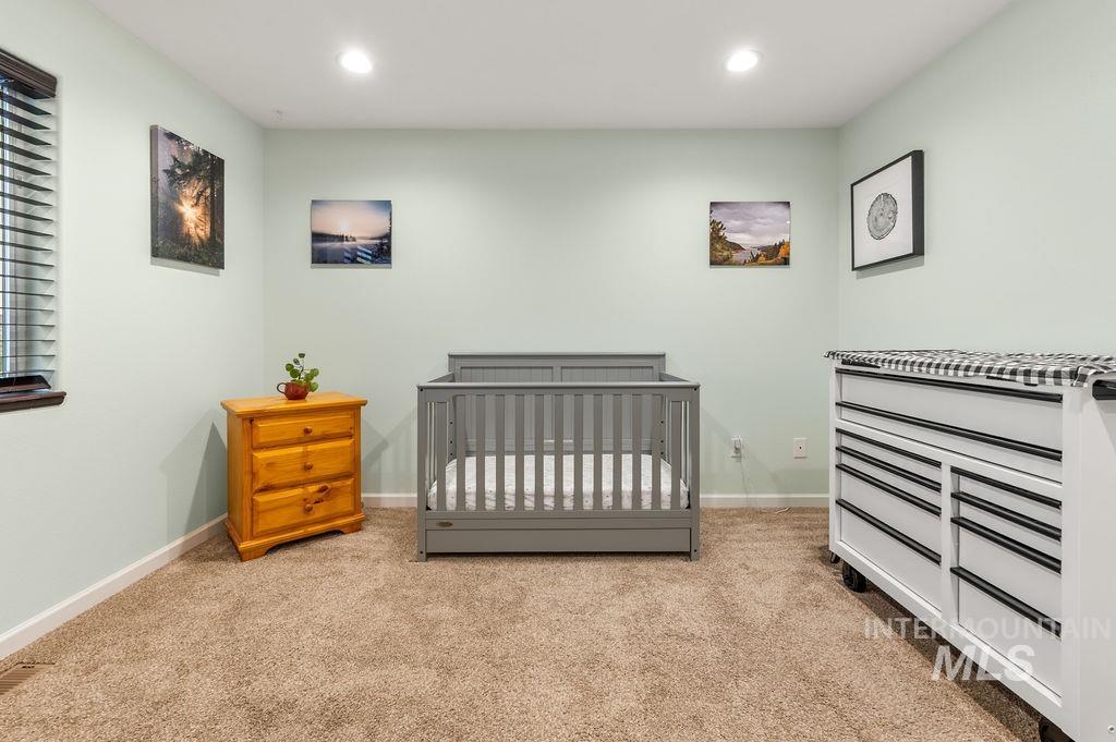 Nursery with a gray crib, tan carpet, and wooden dresser.