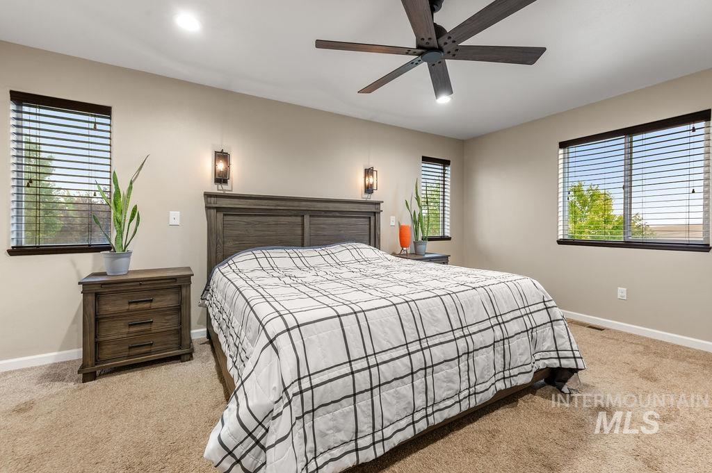Bedroom with a large bed, dark wood furniture, beige carpet, and windows with blinds.