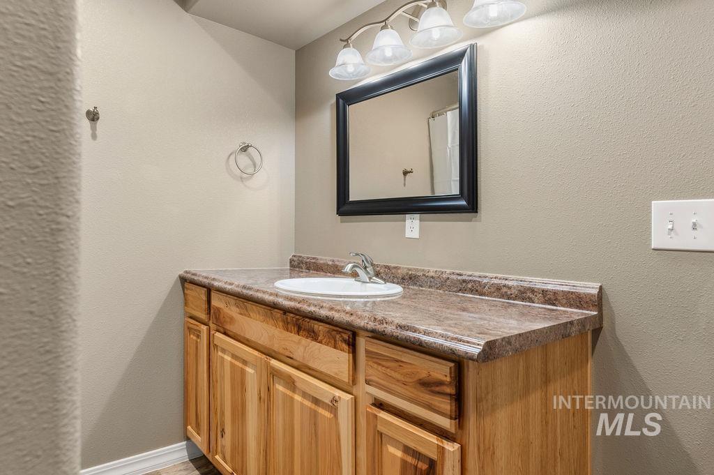 Bathroom vanity with a white sink, marbled countertop, and honey-colored wood cabinets.