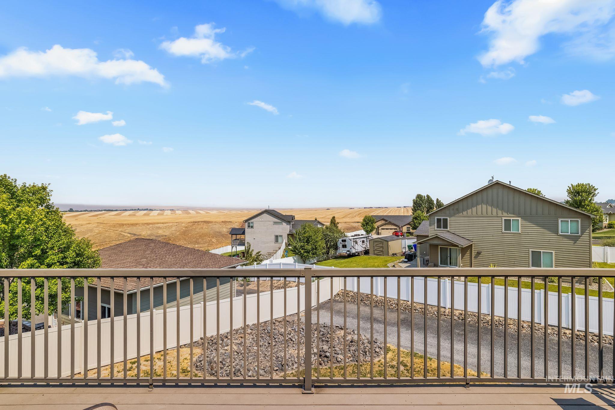Deck view across neighboring homes and fenced yards toward open golden fields.