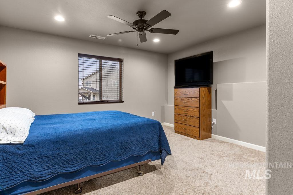 Bedroom with a blue bedspread, ceiling fan, and wooden dresser topped by a television.