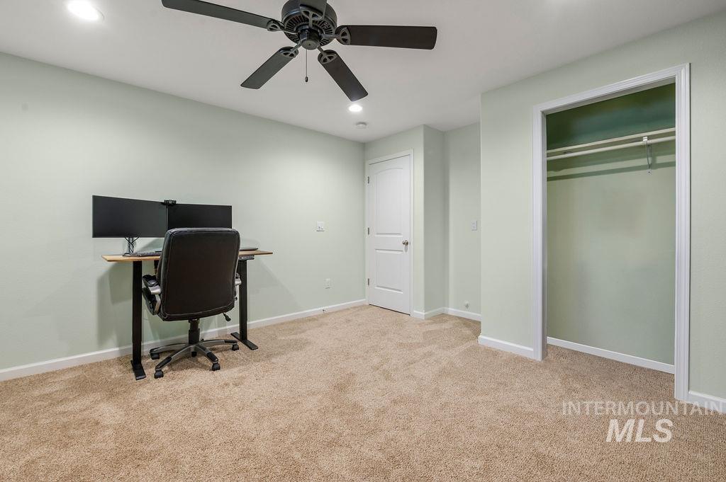 Carpeted home office with a desk and chair beside an open closet.