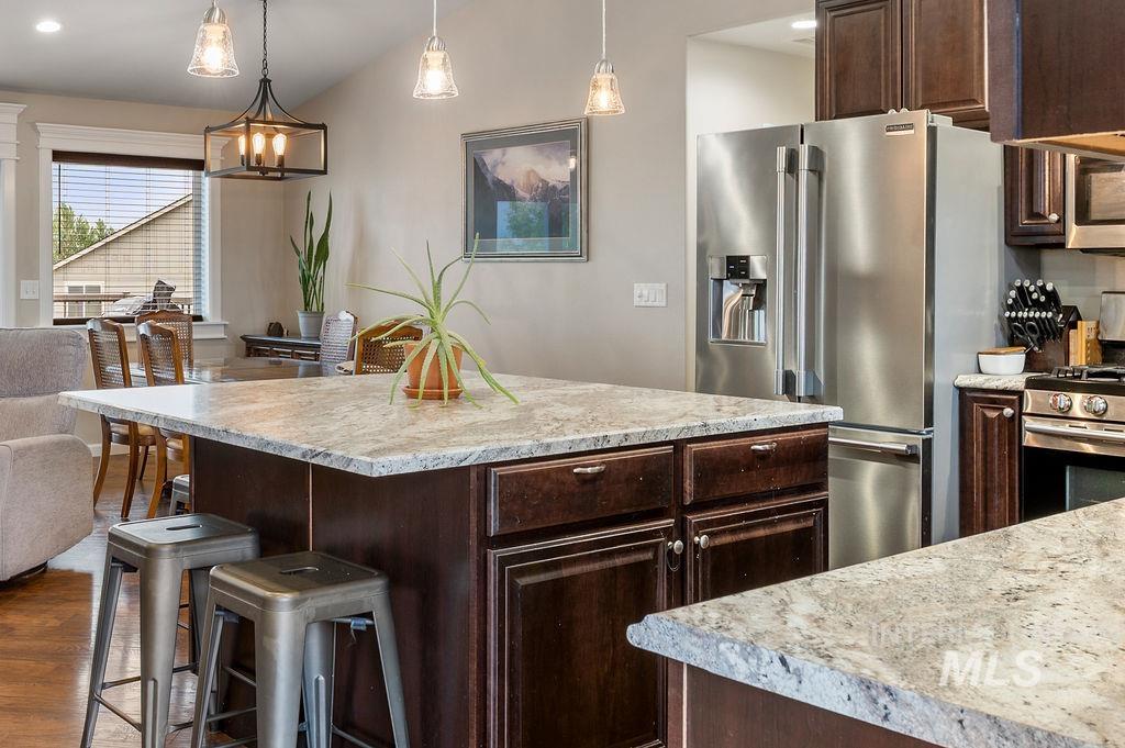 Kitchen with a granite island, dark wood cabinets, stainless steel appliances, and pendant lights.
