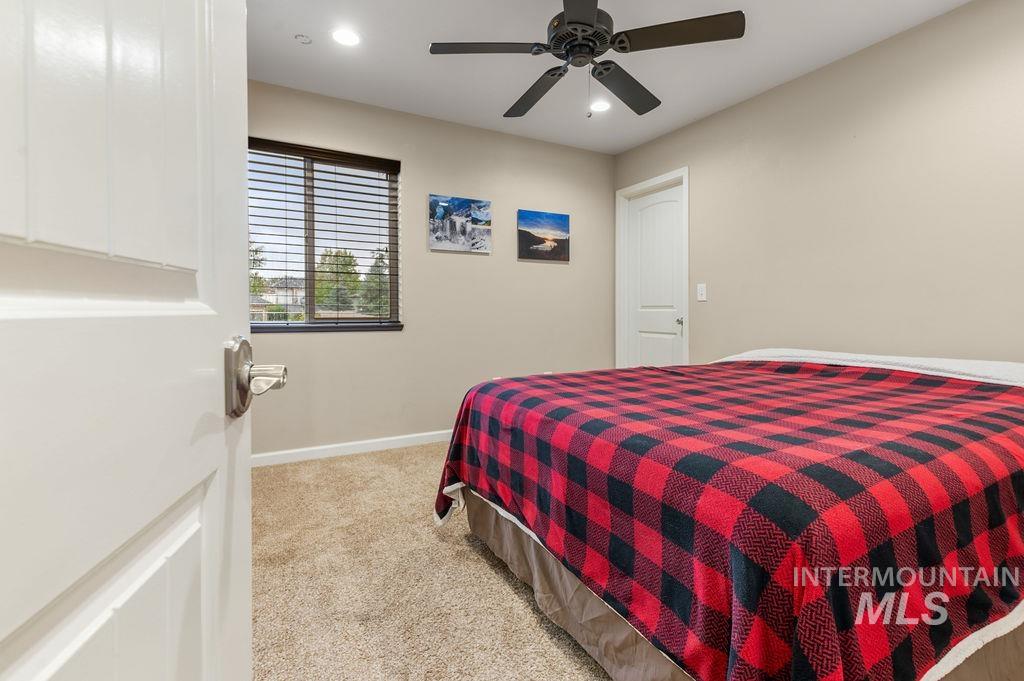 Bedroom with a red-and-black plaid bedspread, beige carpet, and a ceiling fan.