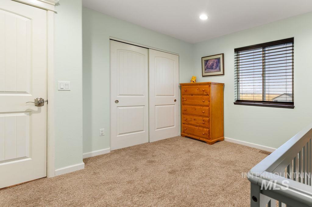 Carpeted upstairs room with white closet doors, a wooden dresser, window blinds, and stair railing.