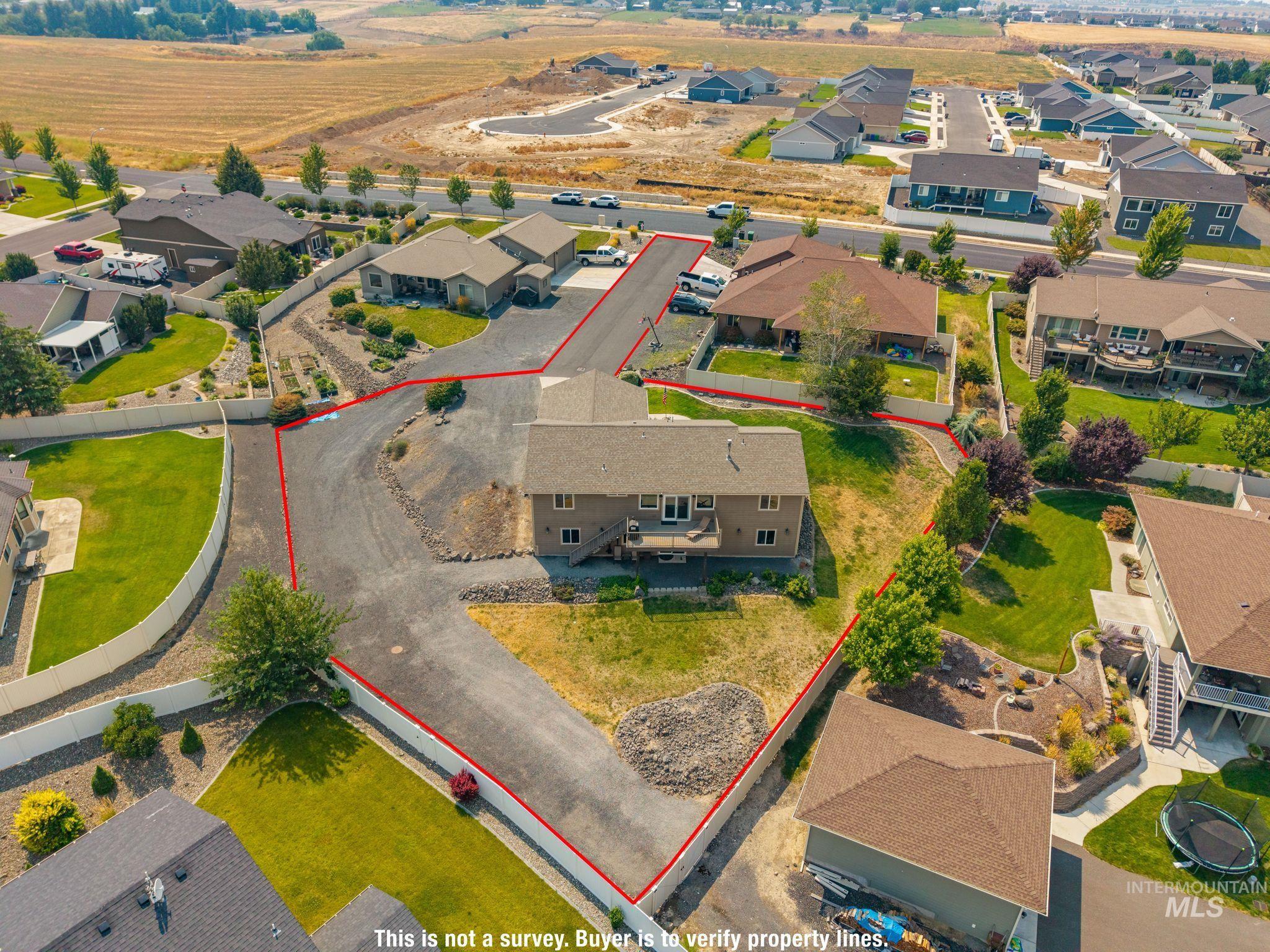 Aerial view of a house and large paved lot outlined in red among neighboring homes.