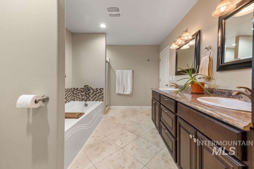 Bathroom with double vanity, tiled floor, soaking tub, and glass-enclosed shower.