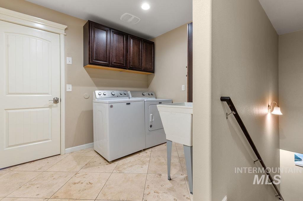 Laundry room with a washer and dryer beneath dark wood cabinets and a beige tiled floor.