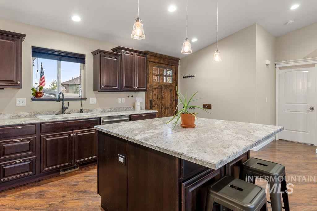 Kitchen with dark wood cabinets, a large stone island, pendant lights, and hardwood floors.