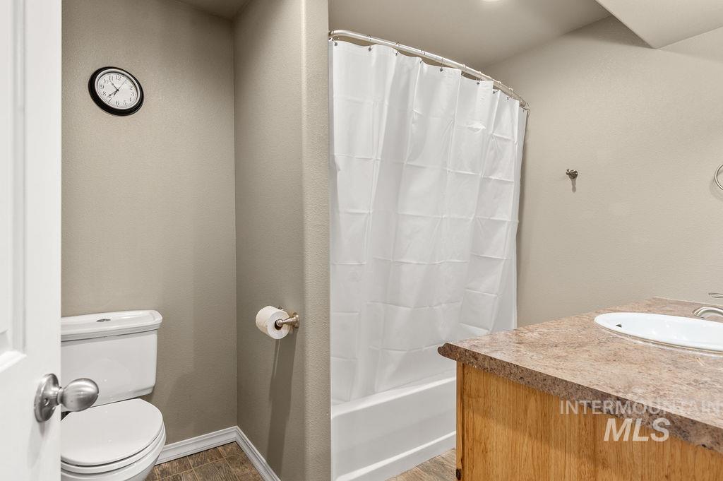Bathroom with a white shower curtain, toilet, and wood vanity with a mottled countertop.