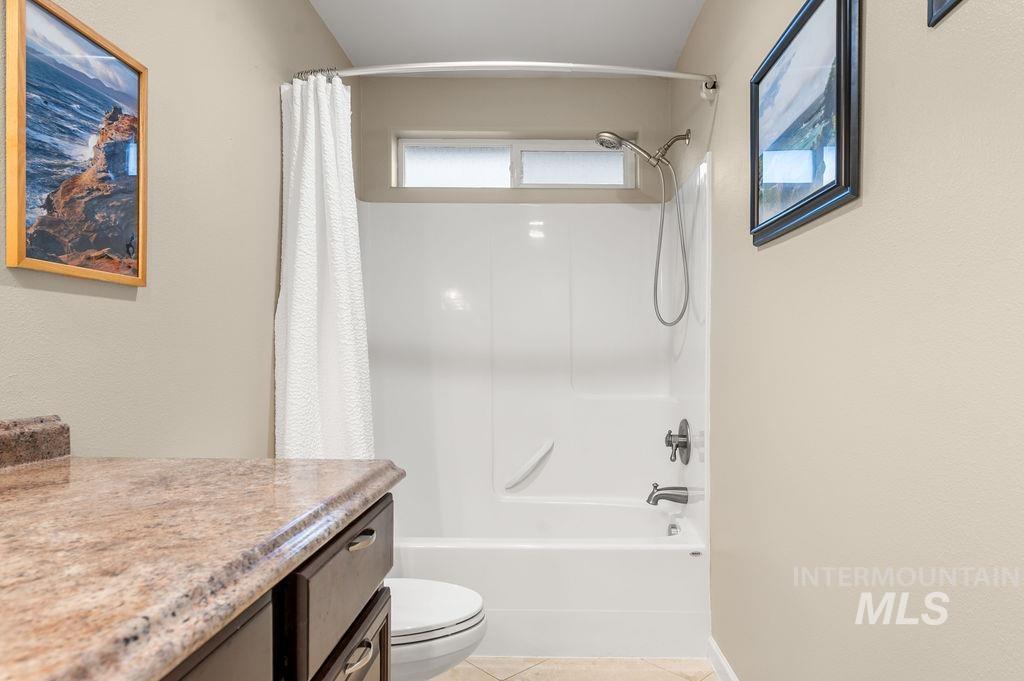 Bathroom with a white tub and shower, granite vanity, and framed coastal photographs.