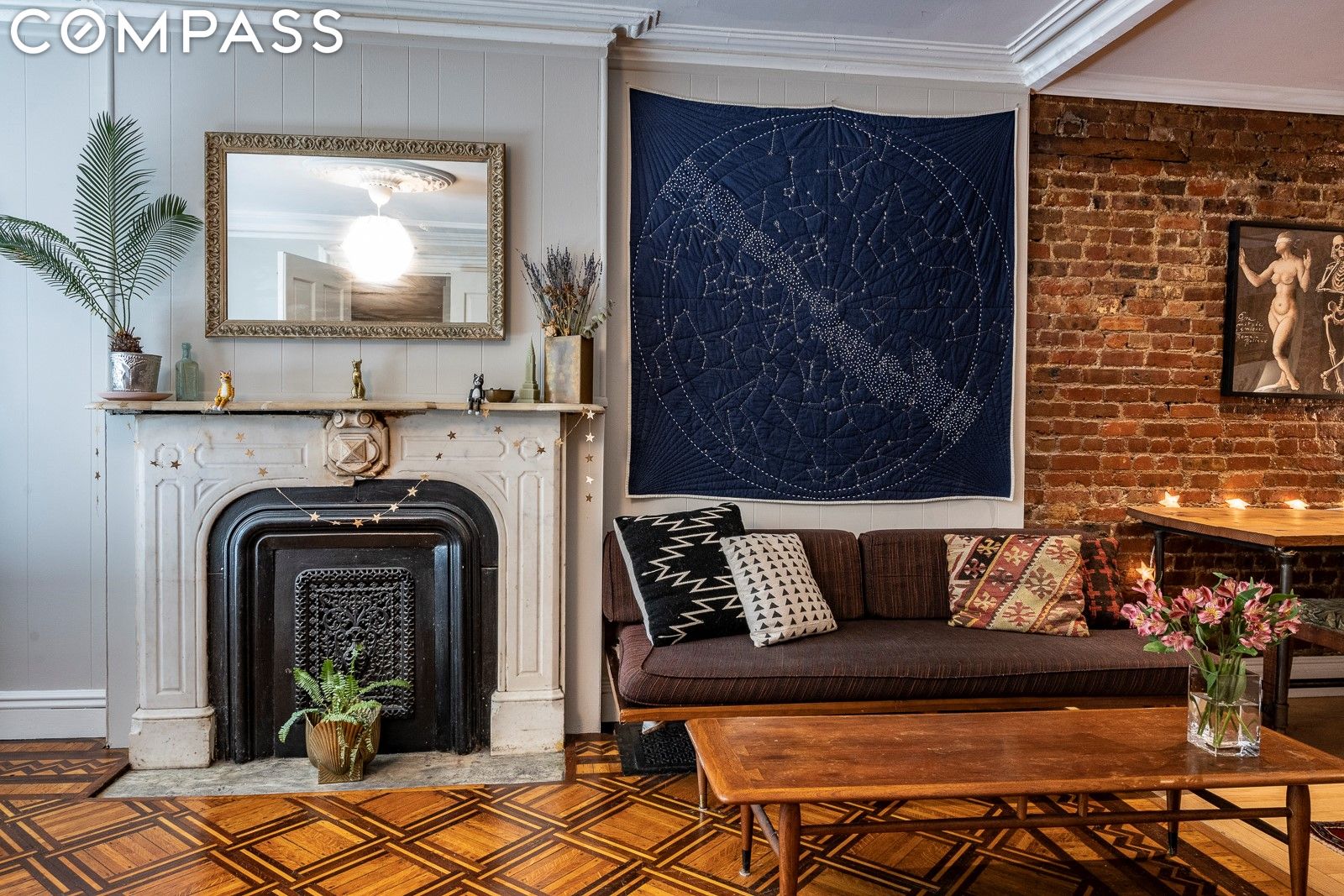 Living room with ornate fireplace, dark sofa, star-map wall hanging, and patterned parquet floor.