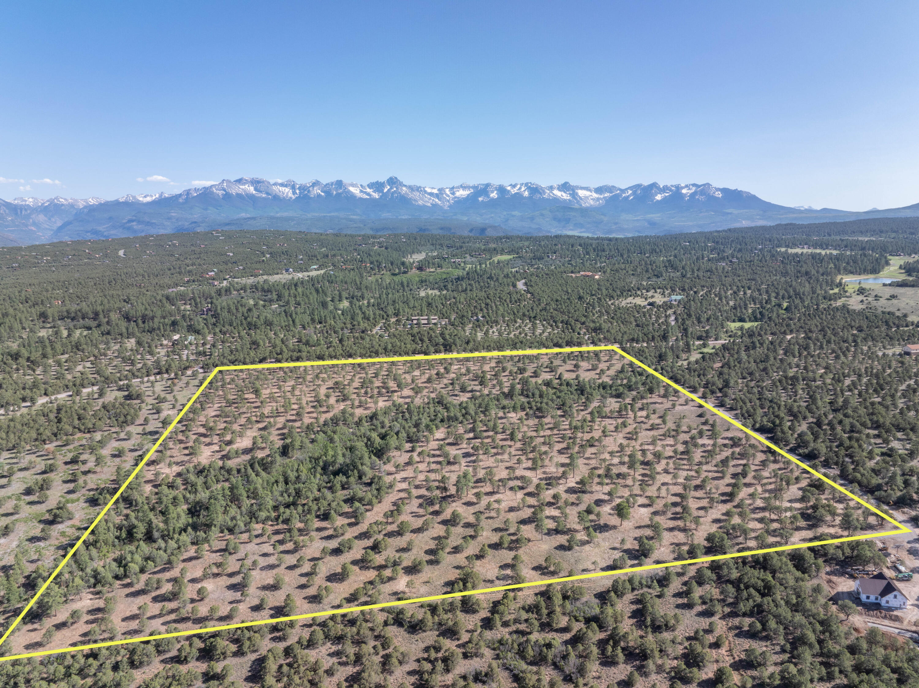 Aerial view of a wooded vacant parcel outlined in yellow, with snow-capped mountains beyond.