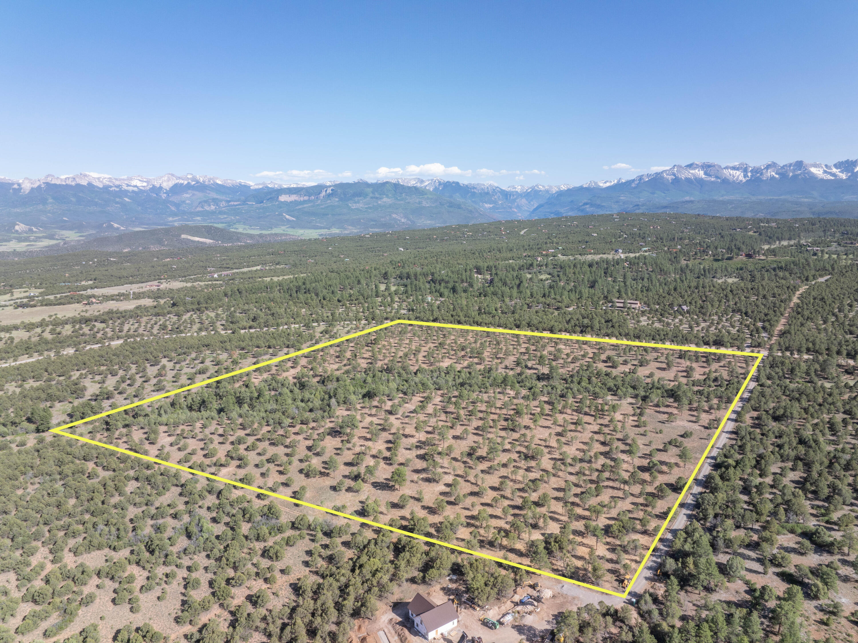 Aerial view of a tree-dotted parcel outlined in yellow, with a road and snow-capped mountains beyond.