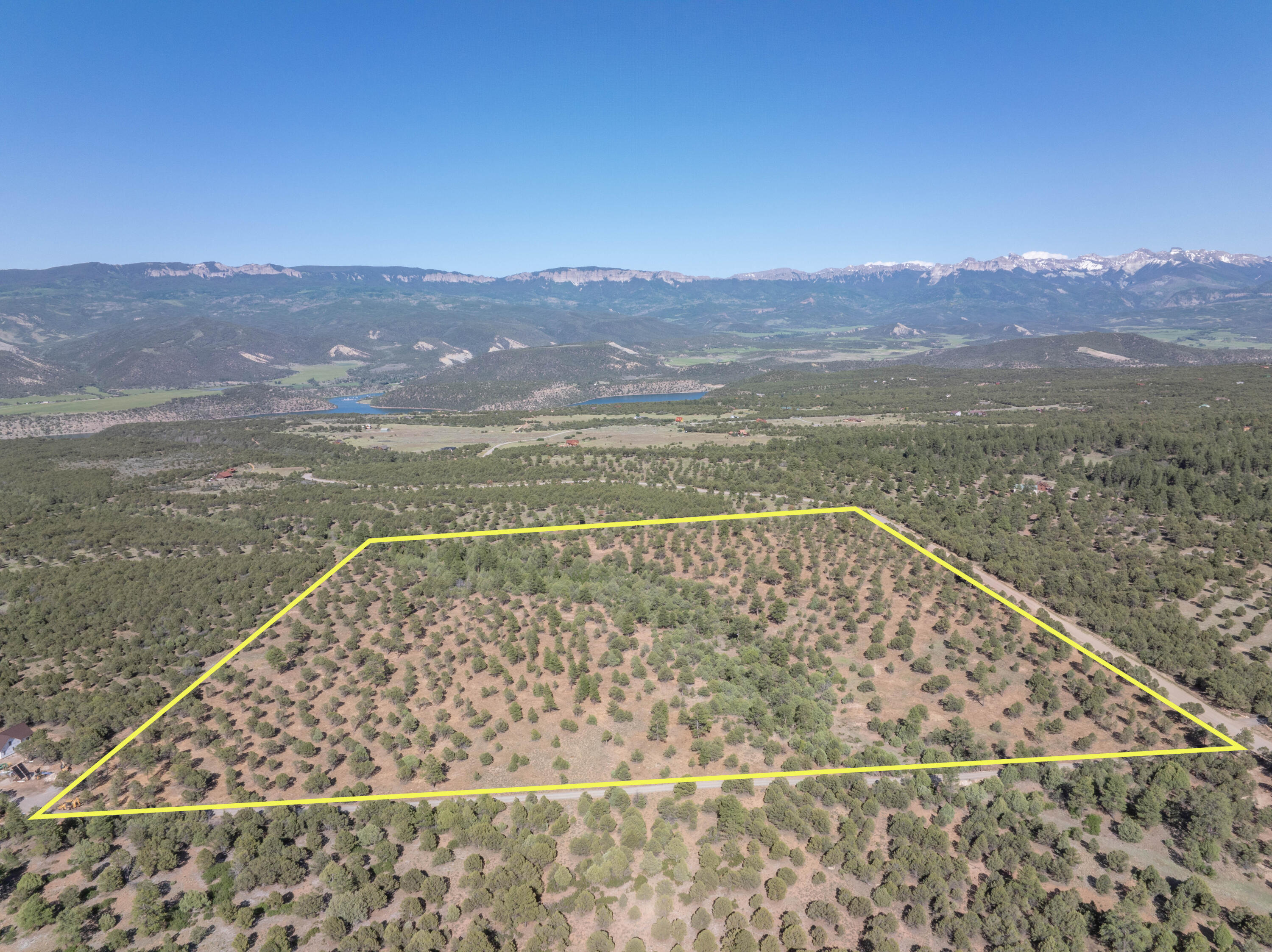 Aerial view of a tree-dotted parcel outlined in yellow, with a lake and mountain ranges beyond.
