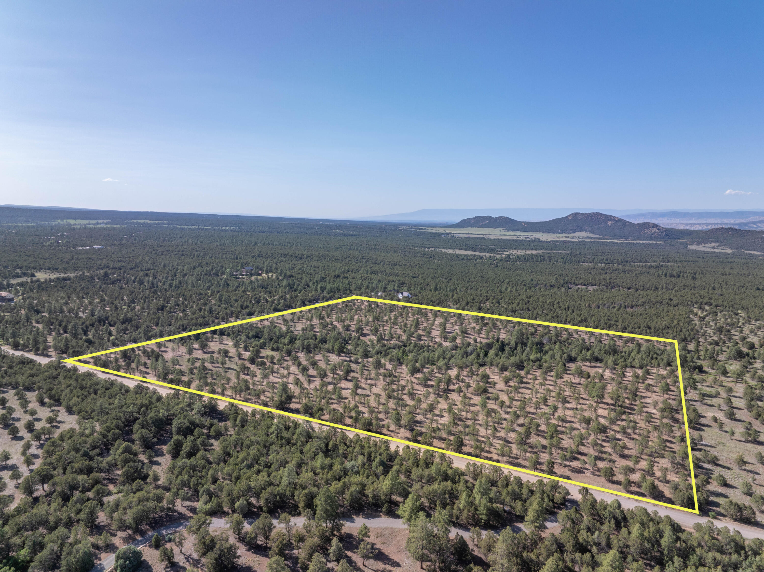 Aerial view of a tree-covered property outlined in yellow beside a road, with distant hills beyond.