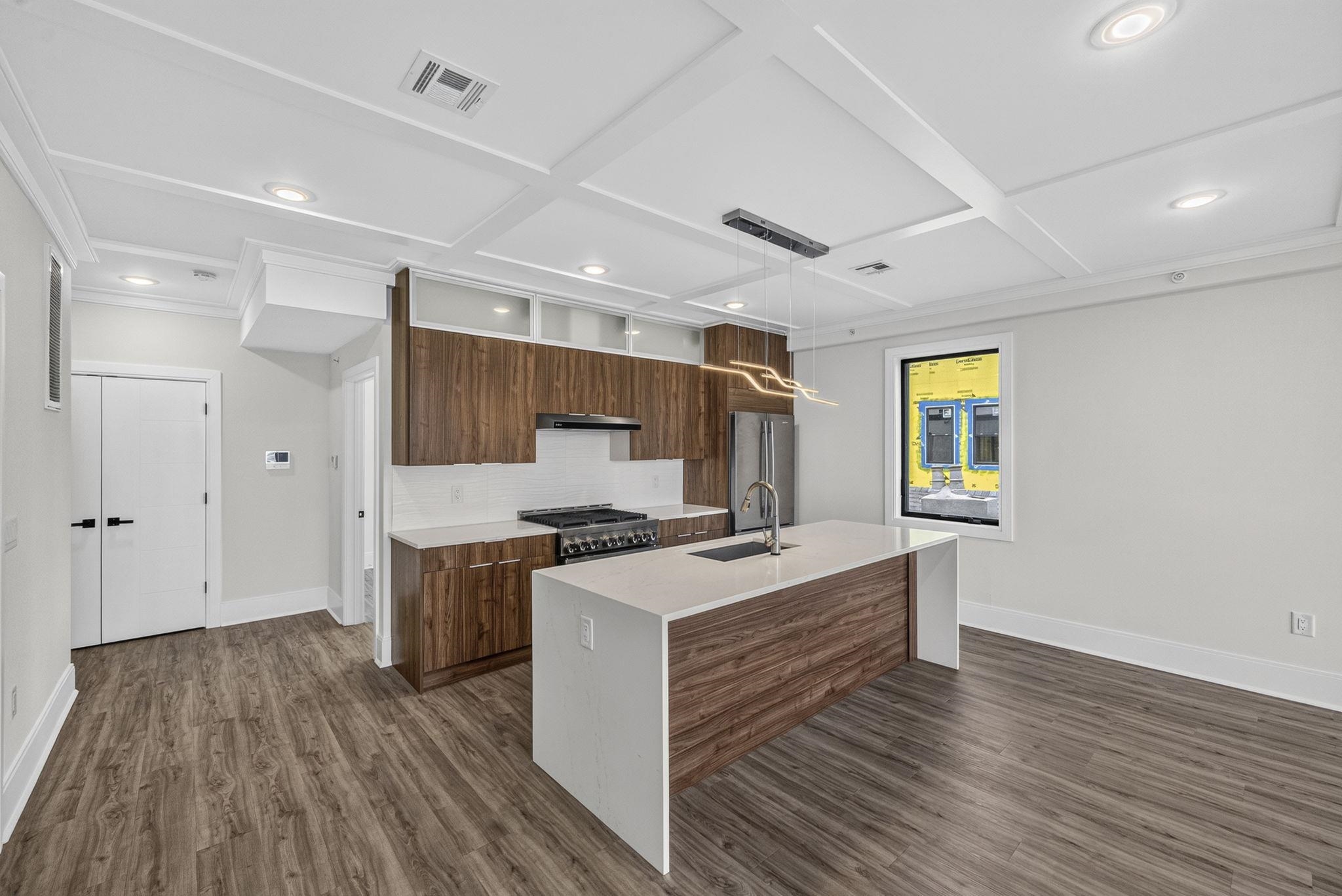 Modern kitchen with walnut cabinets, a large white island, stainless appliances, and wood-look flooring.