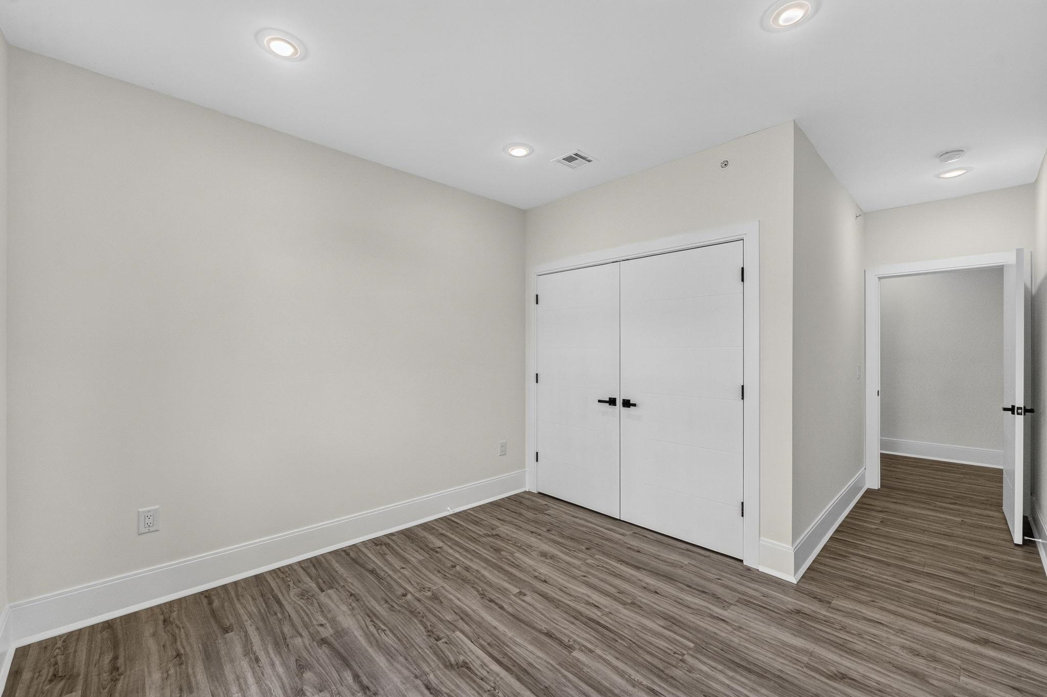 Empty room with wood-look flooring, recessed lights, and white double closet doors.