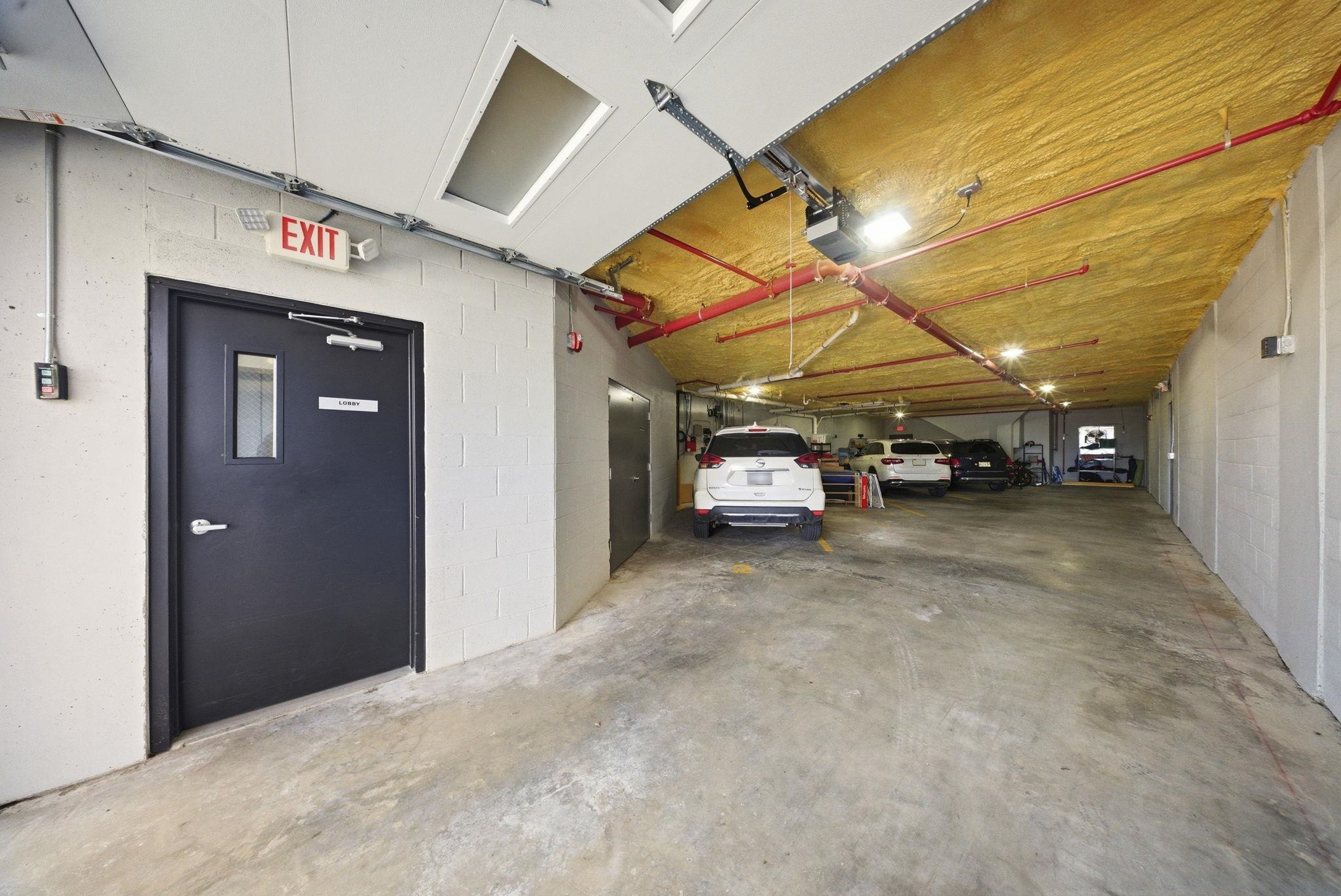 Building parking garage with parked cars, exposed sprinkler pipes, and a lobby entrance.