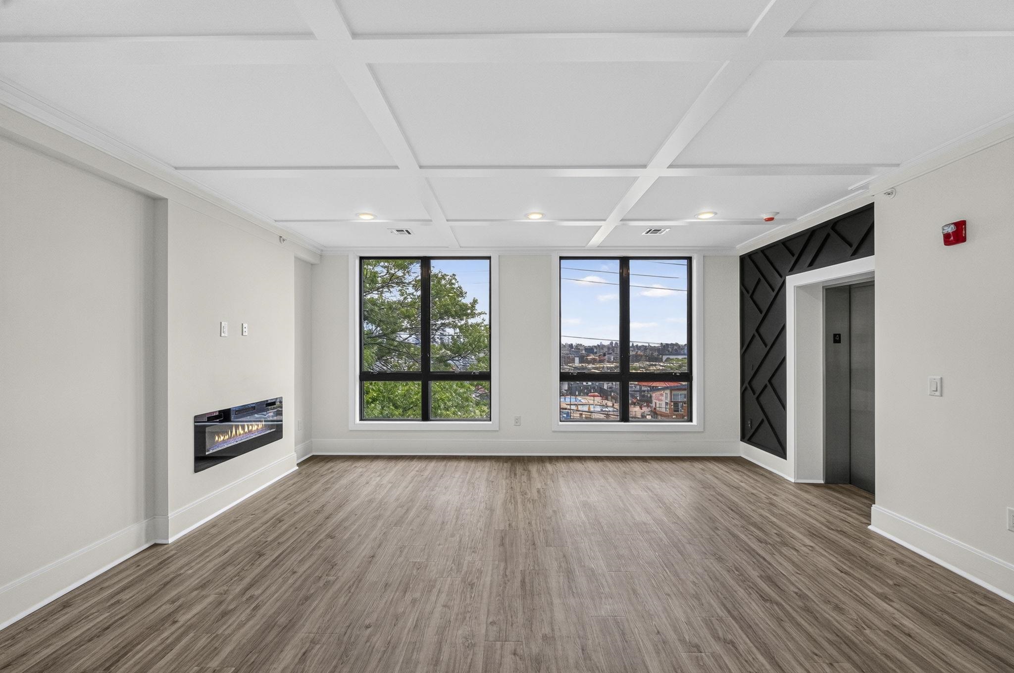 Empty lounge with a wall-mounted fireplace, large windows, and an elevator beside a black accent wall.