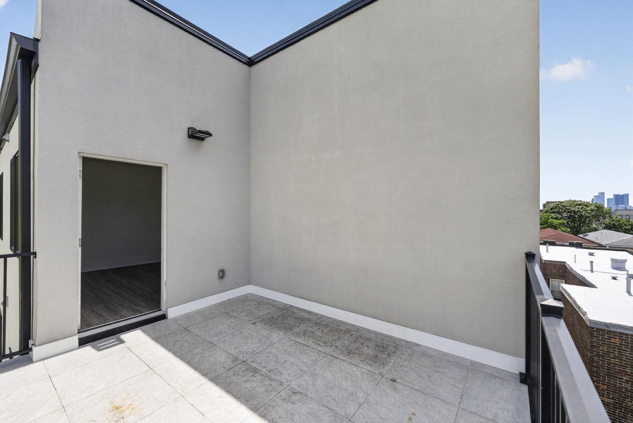 Rooftop terrace with gray tile flooring, black railings, and distant high-rises.