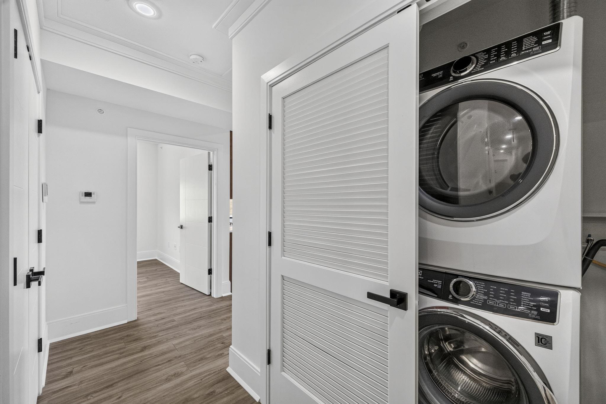 Laundry closet with stacked front-loading washer and dryer behind an open louvered door.