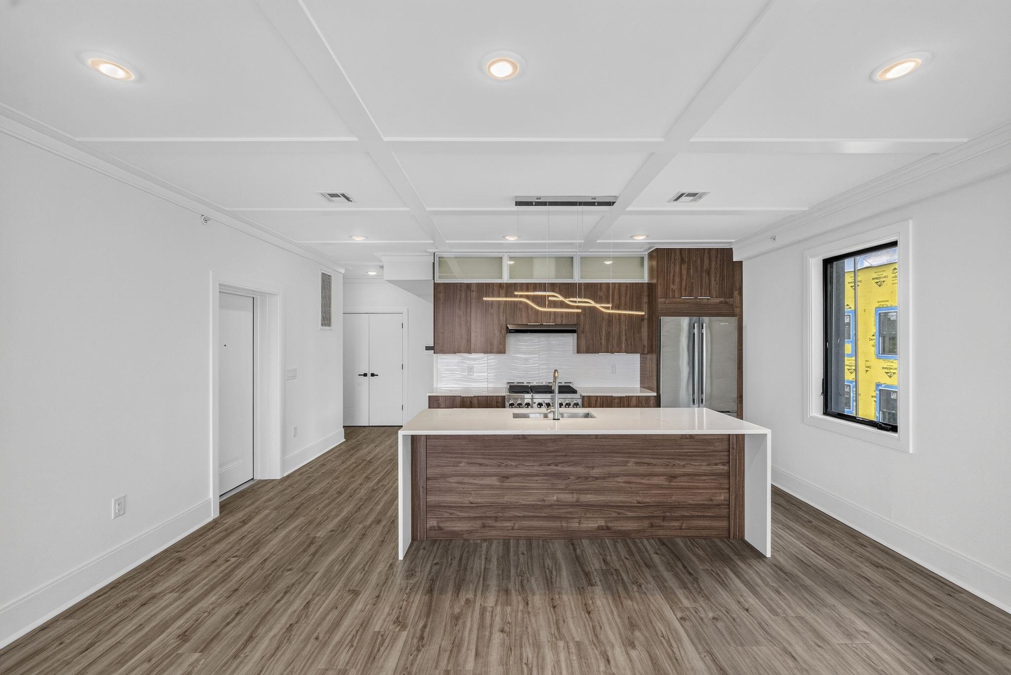 Modern kitchen with a large white island, walnut cabinets, stainless steel appliances, and wood-look floors.