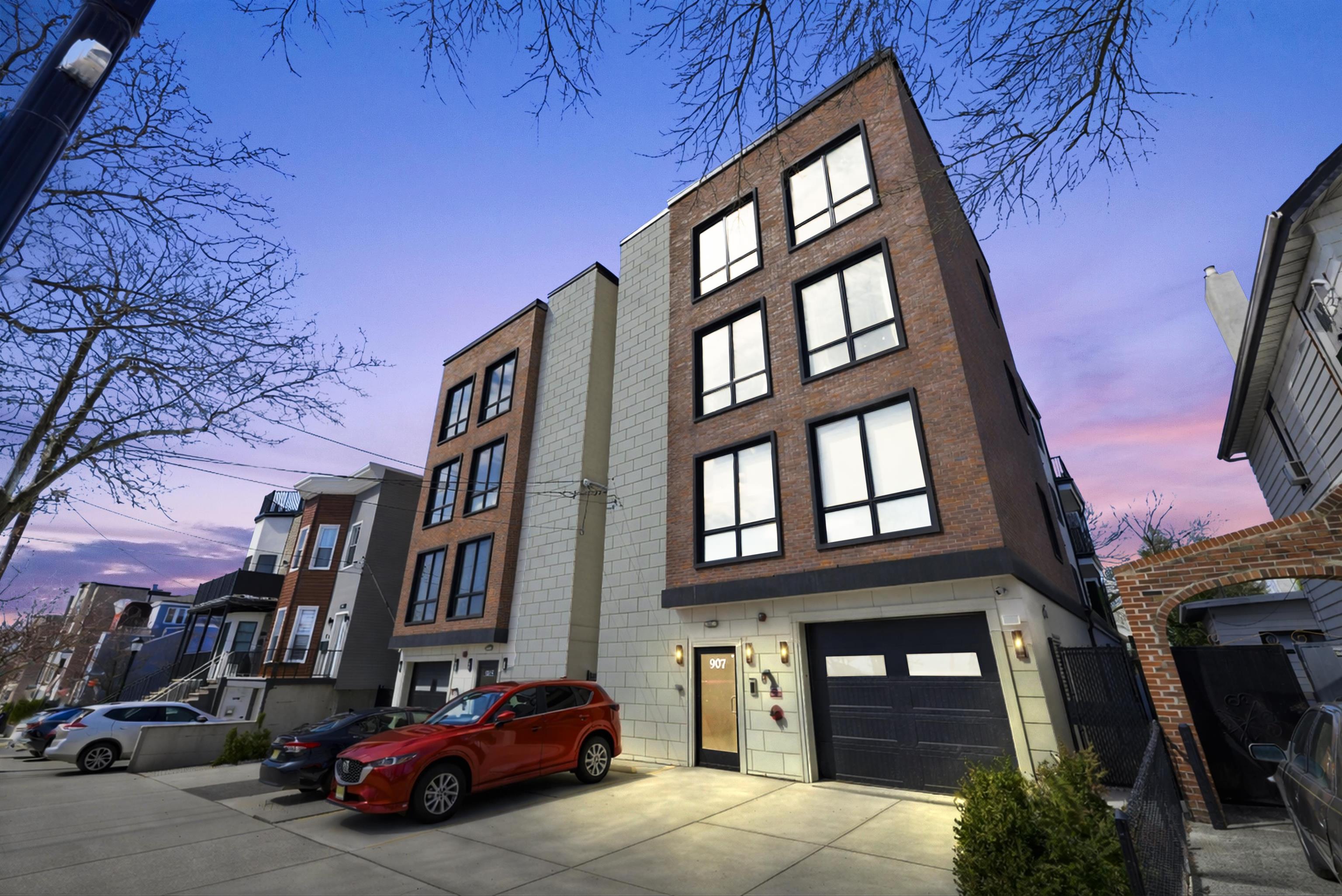 Modern brick residential building with large black-framed windows and a garage at dusk.