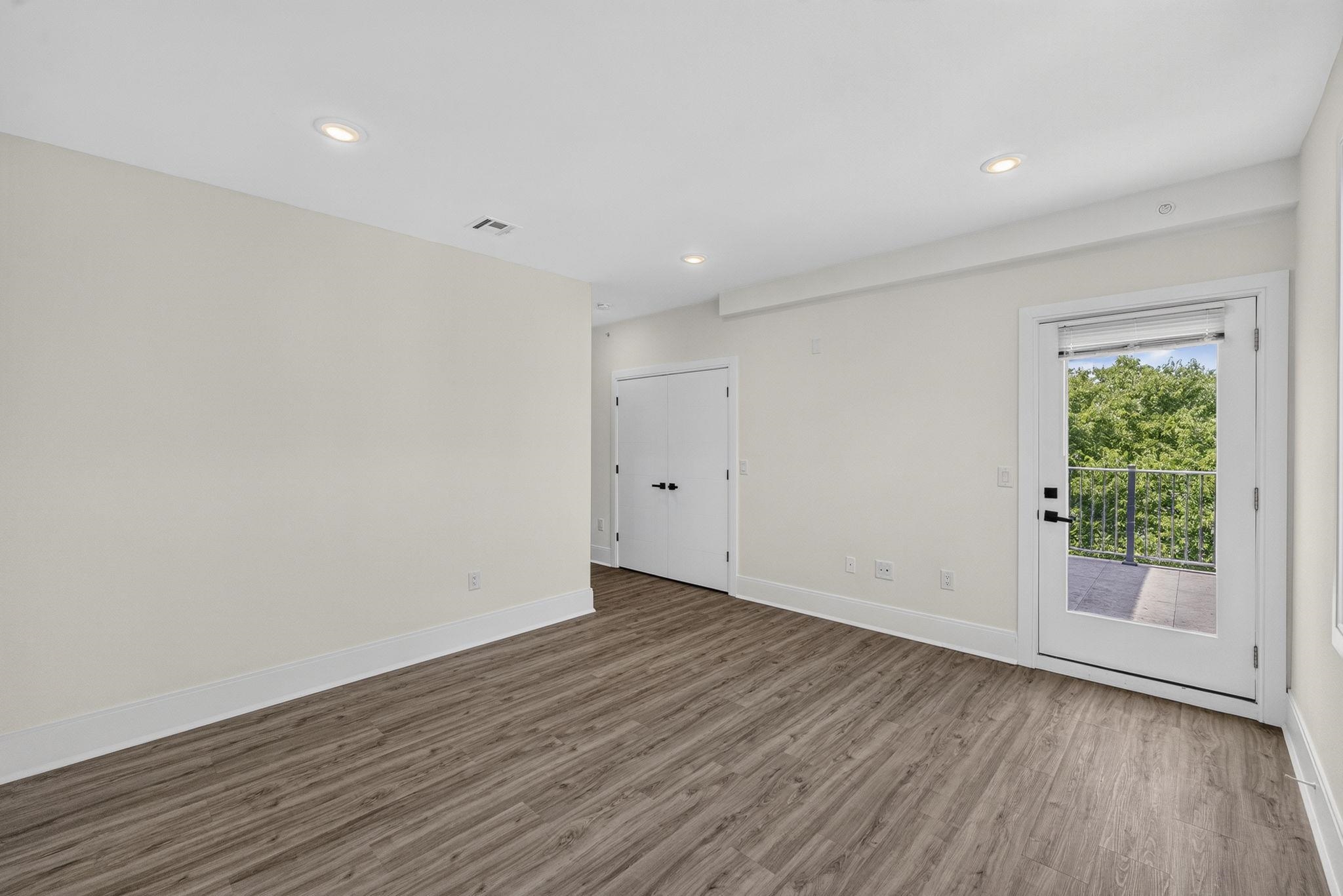 Empty room with wood-look flooring and a glass door opening onto a balcony.