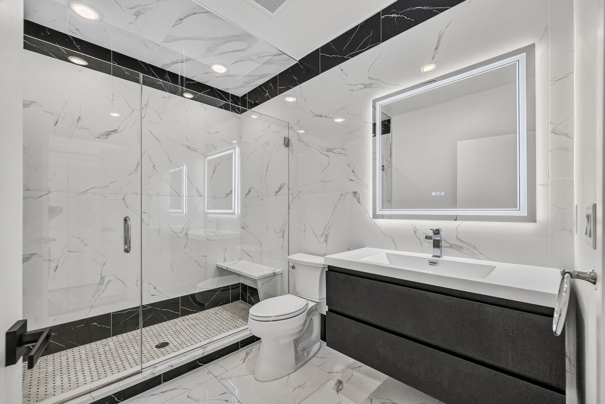 Modern marble-look bathroom with a glass walk-in shower, built-in bench, and dark floating vanity.