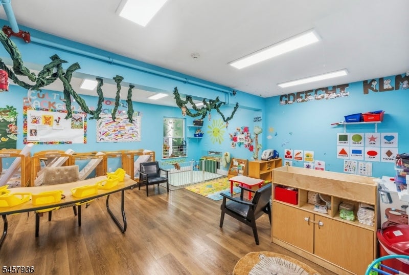 Childcare classroom with turquoise walls, child-sized tables, cribs, and colorful learning displays.