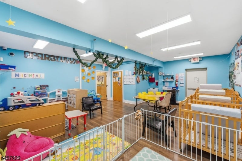 Childcare room with blue walls, wooden cribs, child-sized tables, toys, and a gated play area.