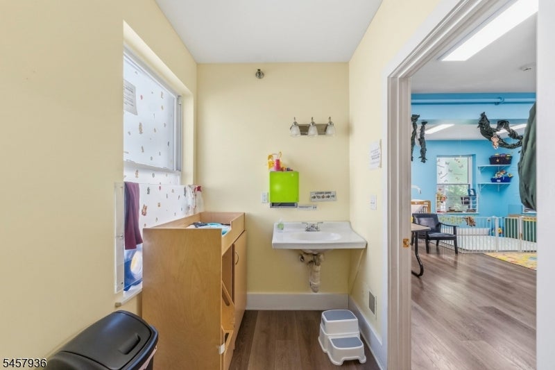 Bathroom changing area with a wall-mounted sink and wooden cabinet, opening onto a bright blue playroom.