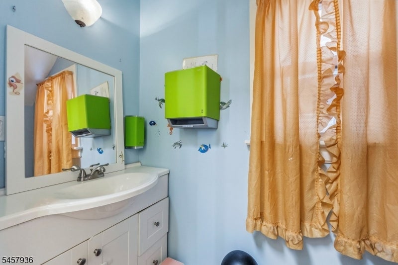 Bathroom with a white vanity, fish-decorated blue walls, green cabinets, and a gold ruffled shower curtain.