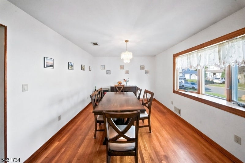 Dining room with a dark wood table, hardwood floors, chandelier, and large lace-curtained window.