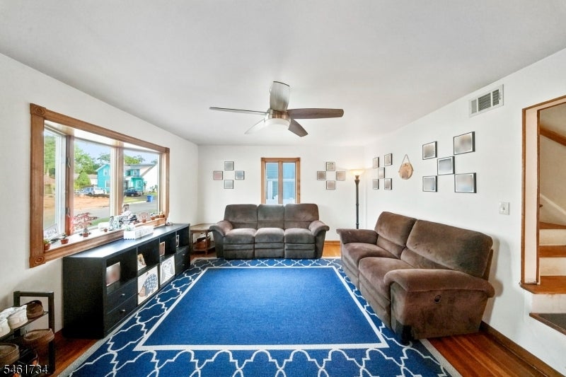 Living room with brown sofas, a blue patterned rug, hardwood floors, and a large window.