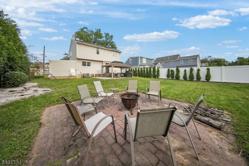 Backyard patio with outdoor chairs around a fire pit, lawn, and white privacy fence.