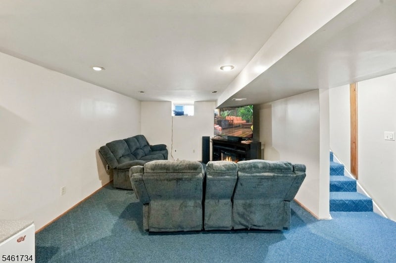 Furnished basement living room with gray sofas, a television above a fireplace, and blue-carpeted stairs.
