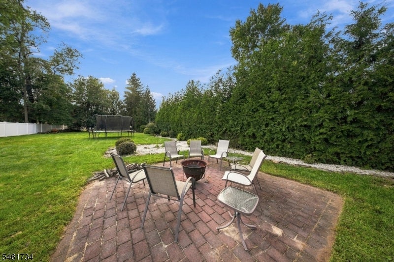 Backyard brick patio with a fire pit and chairs beside a lawn and privacy hedge.